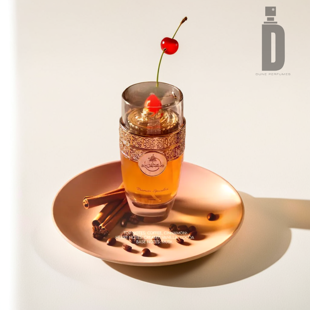 A beautifully adorned Tiramisu Speculoos 100ml EDP bottle by Paris Corner, featuring a golden cap, rests on a reflective copper plate. The bottle, which conveys a dessert-inspired aroma, is embellished with a cherry, cinnamon sticks, and coffee beans. Visible text highlights the Tiramisu Speculoos-inspired fragrance notes.