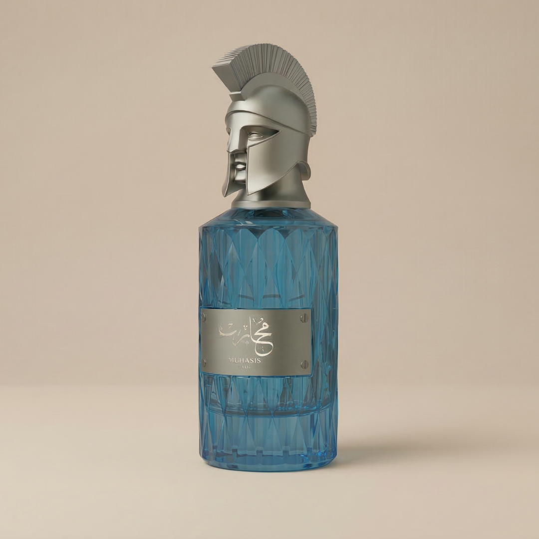 Muharib Hero 85ml EDP by Le Falconé features a blue glass bottle with a silver metal plate and Spartan helmet cap, standing out boldly against a plain beige background—a symbol of dynamic fragrance.