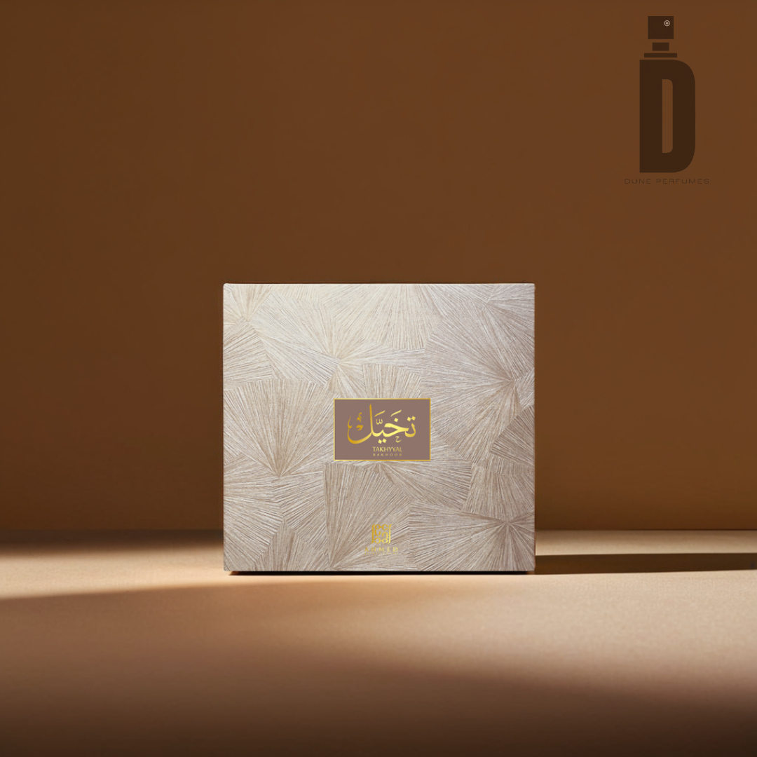 A beige and gold square perfume box with ornate patterns displayed against a light brown background. A gold label on the front features Arabic text in elegant script, hinting at the enchanting scent of Takhyyal Bakhoor (6 tablets) from Ahmed Al Maghribi. The logo for "Ahmed Al Maghribi" is visible in the top-right corner.