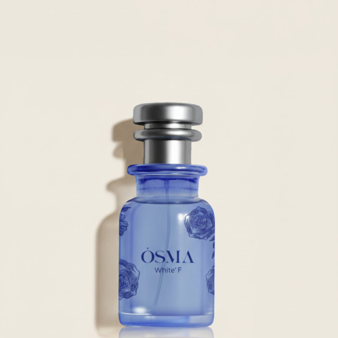 A blue glass "White F 75ml EDP" perfume bottle by Osma, with a silver cap and subtle floral patterns, stands against a beige background, exuding a bright gourmand scent with notes of orange blossom.