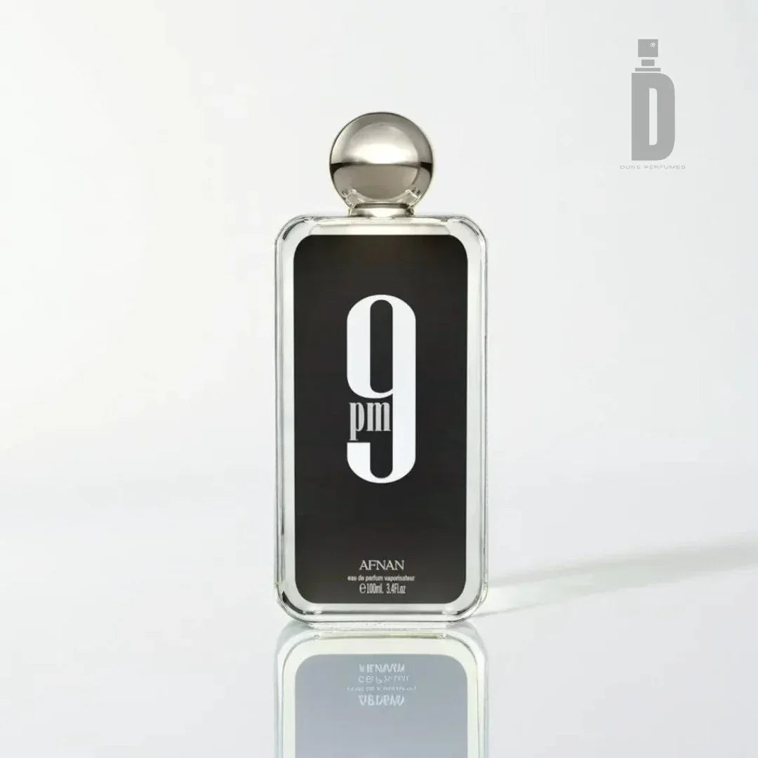 A clear glass bottle of Afnan's "9pm 100ml EDP" perfume, elegantly labeled with bold white text against a black background. The bottle is topped with a silver spherical cap and stands on a sleek, white reflective surface. Hinting at its floral allure, the text reveals the perfume's volume as 100ml (3.4 fl. oz.), promising a truly sensual experience.