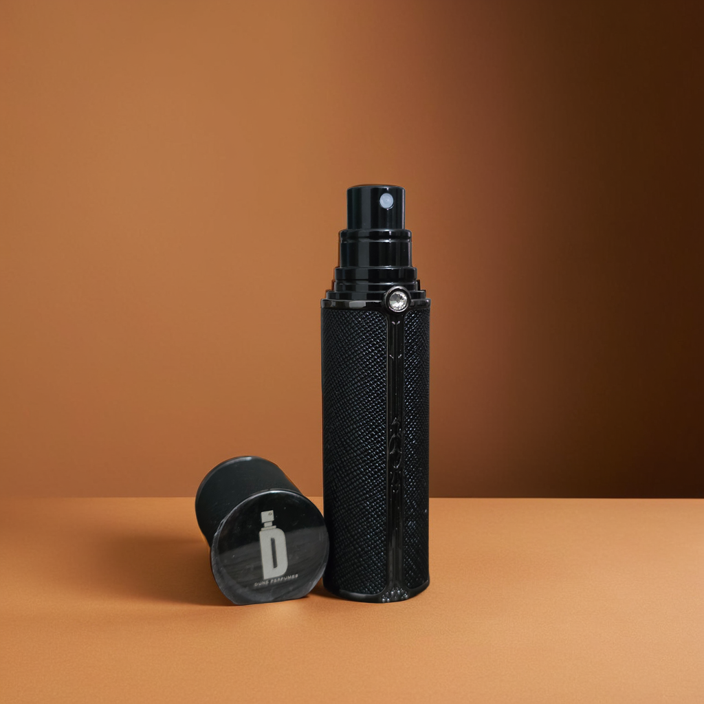 The 5ml & 10ml Travel Spray by Dune Perfumes, in a sleek black refillable bottle with a shiny detached cap, stands upright on a tan surface. The textured design beautifully catches the light against the warm brown background.