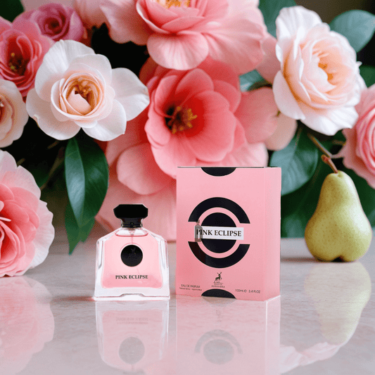 The Pink Eclipse 100ml EDP by Maison Alhambra is shown with its box on a marble surface, adorned with bold black circular designs. Pink flowers and a pear in the background hint at the fragrance’s radiant appeal.