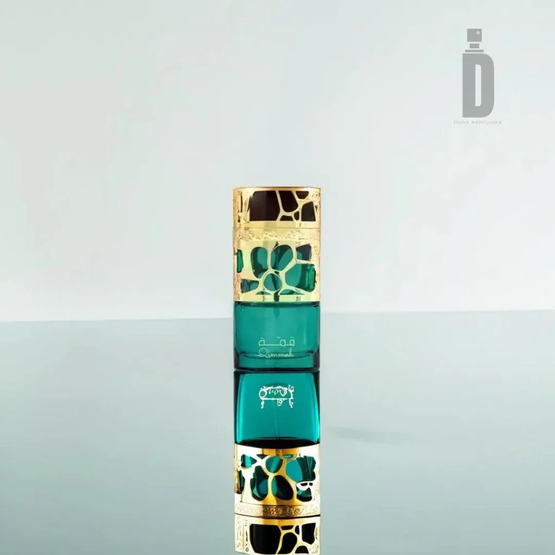 A green and gold perfume bottle with a decorative design sits upright on a reflective surface, showcasing its mirrored reflection below. Evoking femininity, it embodies the essence of Qimmah Women 100ml EDP by Lattafa. The minimalist, light-colored background highlights a logo with a stylized letter "D" in the upper right corner.