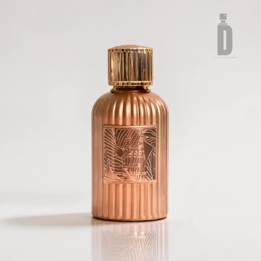 A rose-gold cylindrical perfume bottle with vertical ridges and a detailed decorative label in the center, named Qissa Delicious 100ml EDP - Paris Corner. It features a matching rose-gold cap and is showcased against a clean, light background, capturing sweet moments. A minimalist logo and text are placed in the top right corner under the brand name Paris Corner.