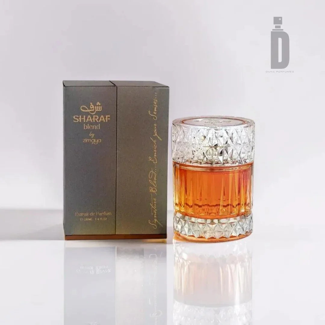 A bottle of Sharaf Blend 100ml EDP by Zimaya is displayed next to its dark gray and gold packaging. The bottle features a clear, intricately designed glass container filled with amber-colored liquid and a textured, matching crystal-like cap, exuding an air of opulence.