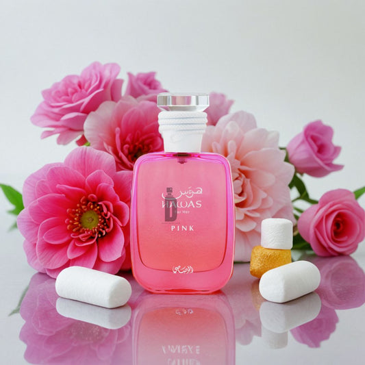 A pink "Hawas Pink 100ml EDP" perfume bottle by Rasasi is showcased among vibrant pink flowers, with white and yellow cylindrical accents surrounding this sweet floral scent on a white surface.