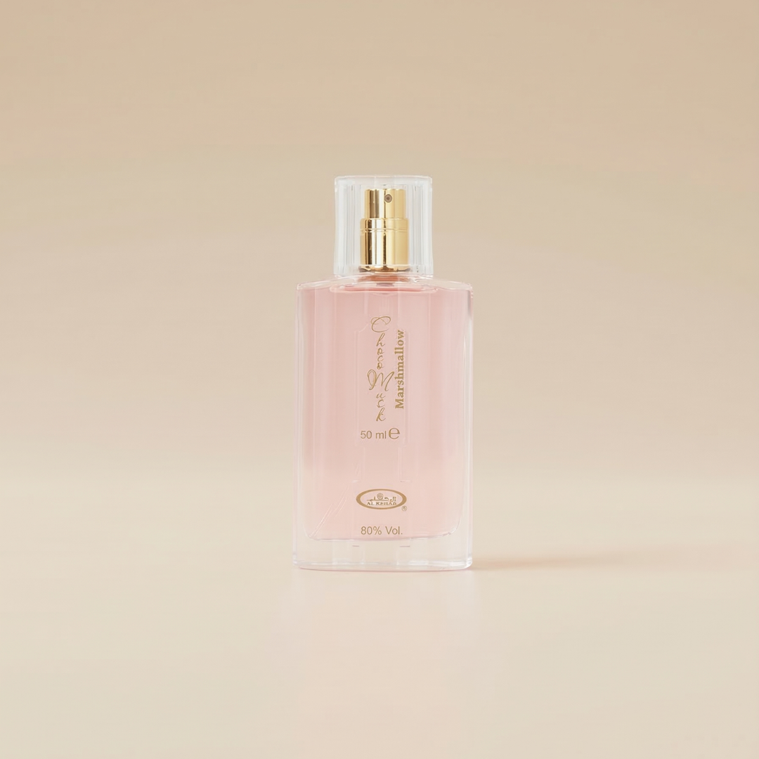 A clear glass Choco Musk Marshmallow - Al Rehab perfume bottle with pink liquid and a gold spray nozzle, featuring gold writing, stands upright on a light beige surface and matching background—perfect for showcasing this sweet Al Rehab fragrance.