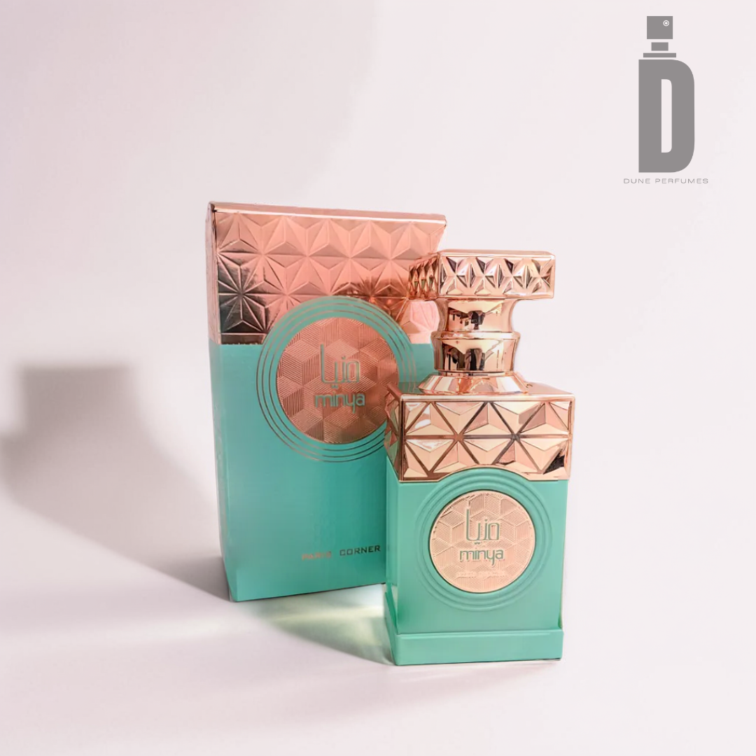A perfume bottle and box set against a light background highlight geometric patterns in gold and teal. The fragrance, "Minya 100ml EDP" by Paris Corner, exudes nutty accords. The logo is elegantly placed in the top right corner, completing this tasteful display of sophistication.