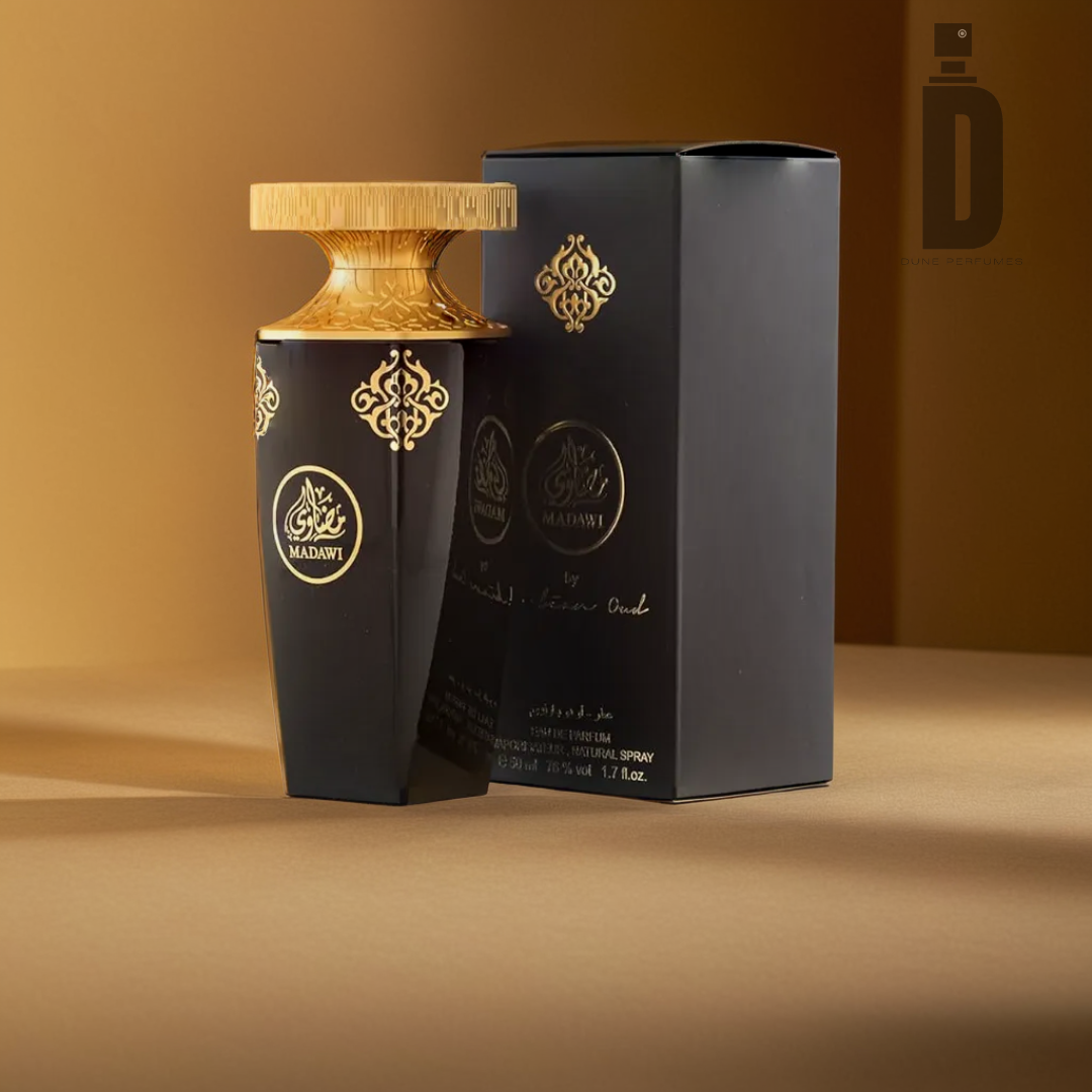 A bottle of the luxurious "Madawi - Arabian Oud" perfume, crafted by Arabian Oud, stands alongside its matching black box. Adorned with intricate gold details, this sophisticated fragrance showcases elegant and ornate designs while blending notes of musk and patchouli. The scene is set against a warm, golden brown background.