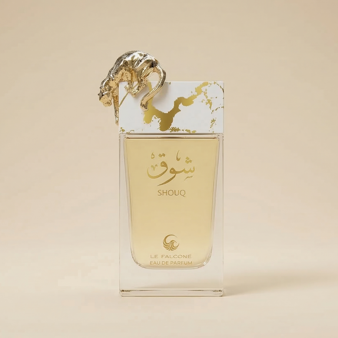 A clear bottle of Shouq 100ml EDP by Le Falconé stands upright, filled with gold liquid. The cap features a decorative gold falcon, adding elegance to this rich gourmand fragrance.