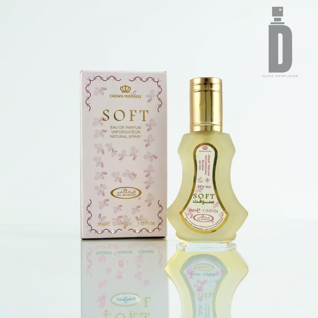 A bottle and box of Al Rehab Soft Eau de Parfum feature a gold-capped, rectangular design with a floral motif on the box. The subtle vanilla fragrance-infused items are set against a plain white background, elegantly casting reflections on the surface.