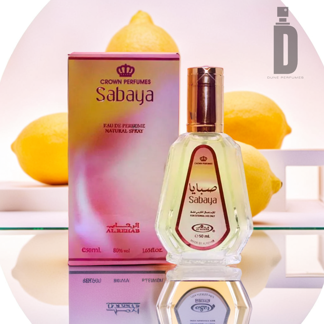 A Sabaya 50ml EDP by Al Rehab and its pink box, featuring elegant branding details, are showcased on a reflective surface. The clear bottle with its golden cap exudes sophistication. Lemons in the background heighten the citrus and floral notes of the fragrance, bringing a fresh and vibrant ambiance to the display.