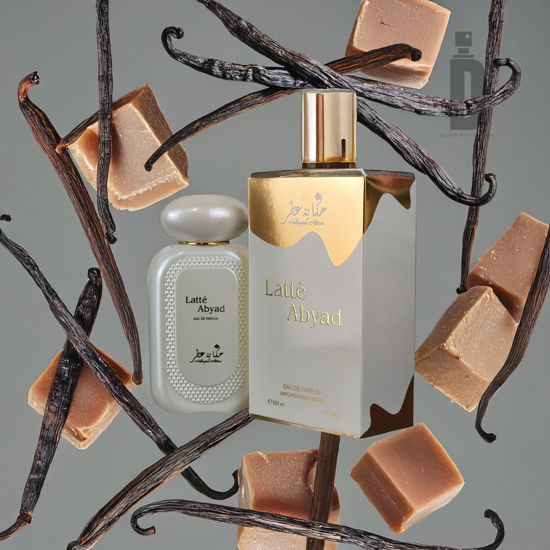 Two Hekayat Attar Latte Abyad 100ml EDP bottles, wrapped in vanilla and caramel scents, one with a gold-capped rectangle shape and the other oval, rest on a soft gray backdrop with the brand's logo subtly placed in the top right corner.