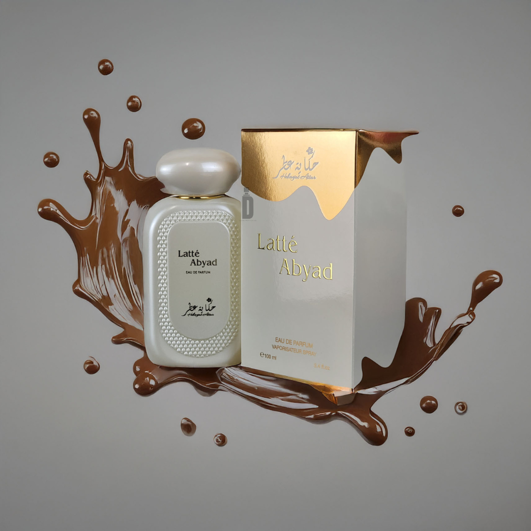 The "Latte Abyad 100ml EDP - Hekayat Attar" fragrance bottle and box, adorned with Arabic script, rest against a splash of brown. The white bottle with a rounded cap complements the cream-and-gold patterned box from Hekayat Attar, promising creamy indulgence in every scent.