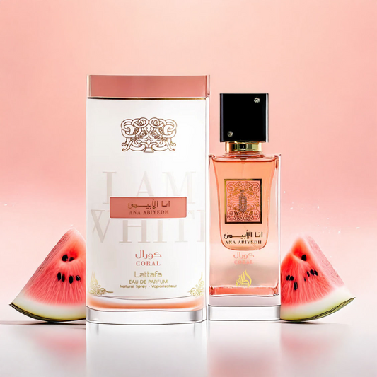 A pink gradient background showcases two "Ana Abiyedh Coral" bottles from Lattafa. The larger, rectangular bottle with a gold cap complements the smaller, square bottle with a black cap. Watermelon slices add a sun-kissed tropical vibe to this floral fragrance setting.