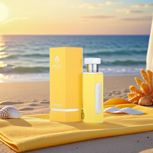 The "Summer Yellow 100ml EDP - Reef" perfume bottle and matching box are on a beach towel, with hints of orange blossom. Seashells and coral embellish the setting as the sun sets over a tranquil ocean in the background.