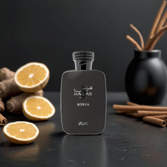 The Hawas Kobra 100ml EDP by Rasasi stands on a dark surface, surrounded by halved lemons, ginger roots, and cinnamon sticks—its bold essence captured beside a black vase holding more cinnamon sticks.