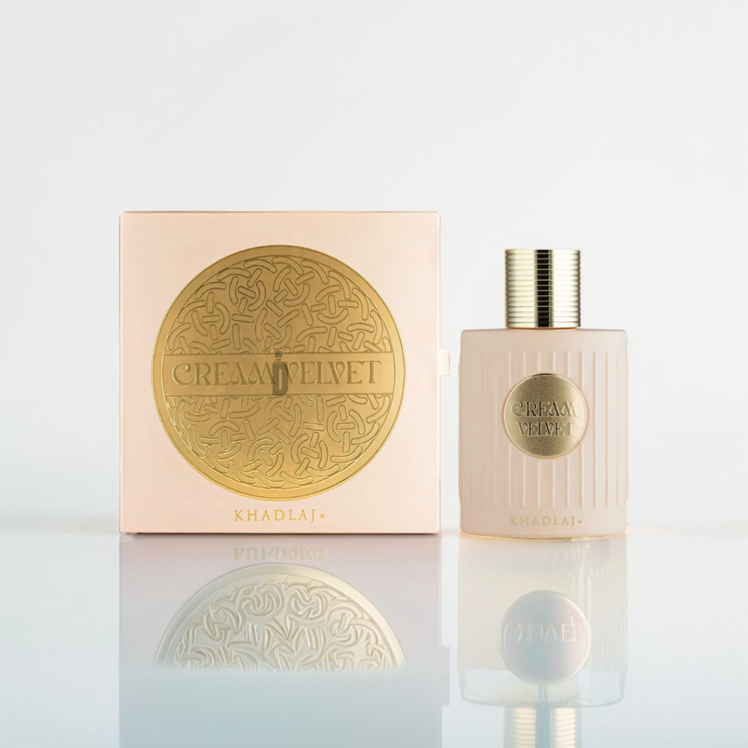 A pink ribbed perfume bottle with a gold cap contrasts elegantly against a soft white background. It stands beside its matching pink and gold box, both adorned with "Cream Velvet 100ml EDP - Khadlaj" in ornate lettering, hinting at the lush vanilla fragrance from the Khadlaj brand within.