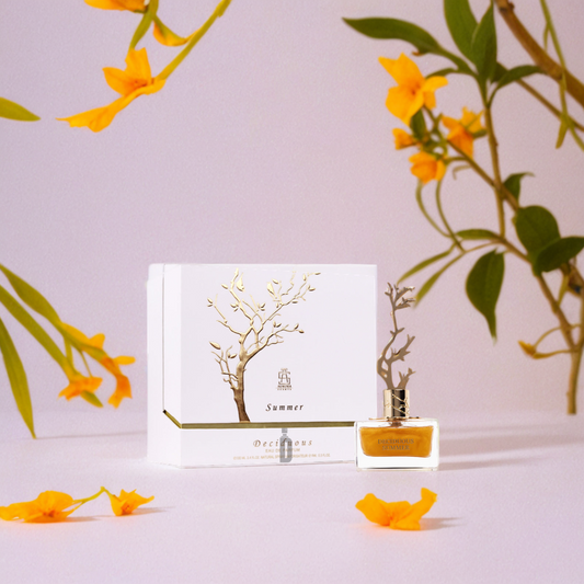 A Deciduous Summer 100ml EDP bottle by Aurora Scents rests in an elegant white box with gold accents on a light surface, surrounded by yellow flowers and green leaves, evoking the fragrance’s radiant, summery allure.