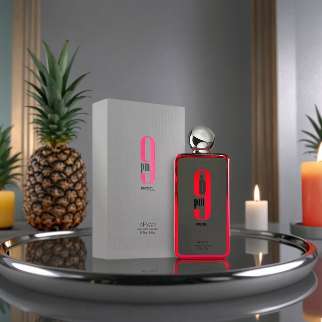 A bottle and box of 9PM Rebel 100ml EDP by Afnan rest on a silver tray with pineapples and candles, highlighting the fragrance's fruity brightness against a neutral background with a framed mirror.