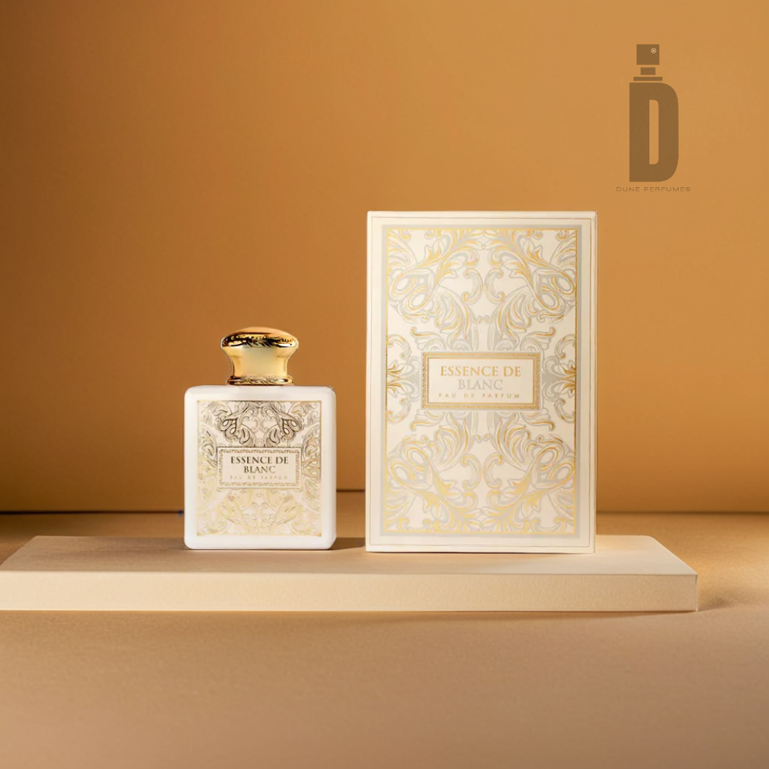 A 100ml bottle of "Essence de Blanc" Eau de Parfum by Fragrance World, adorned with an ornate golden design, is positioned beside its matching box. Set against a warm beige backdrop that enhances its elegant and luxurious appearance, this fragrance exudes captivating notes of ambergris.
