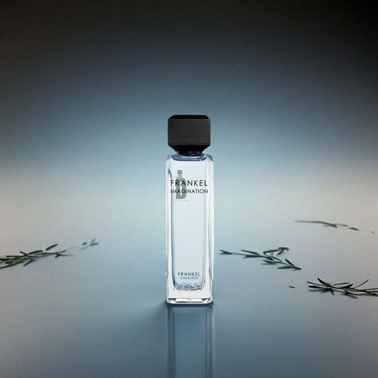 A Frankel Imagination 200ml EDP by Assaf bottle stands upright on a reflective surface, surrounded by small green sprigs with a gradient blue-gray backdrop, capturing the creative essence of this fragrance.