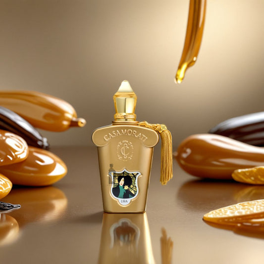 A luxurious gold bottle of Lira Casamorati 100ml EDP by Xerjoff sits on a reflective surface, surrounded by caramel drizzles and dollops with a caramel drop falling above, evoking an indulgent gourmand fragrance in warm golden tones.