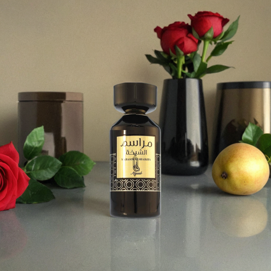 A Marasim Al Shaikha 100ml EDP by Khadlaj stands on a reflective surface, labeled in Arabic, surrounded by a red rose, a pear, two black vases with red roses and green leaves, and a brown jar in the background.