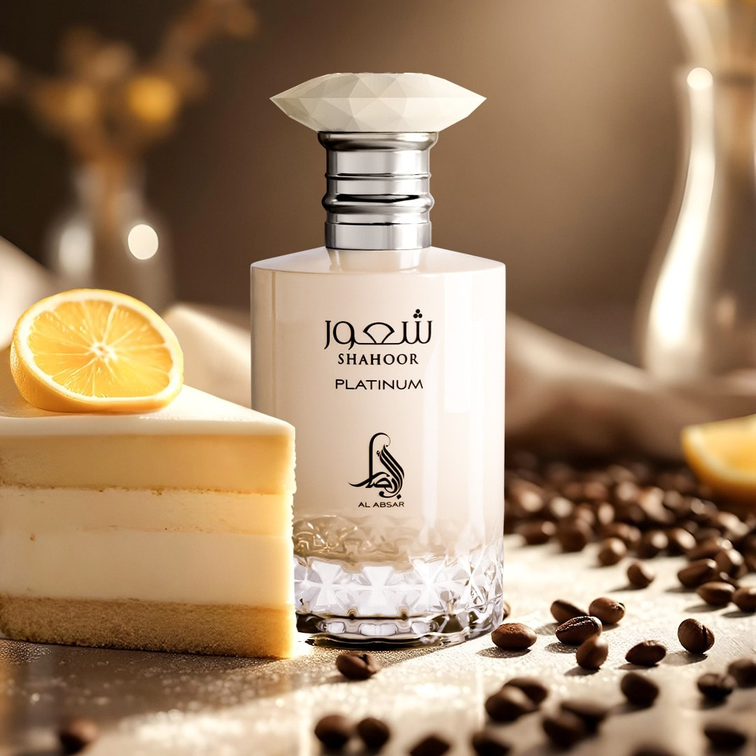 A stylish bottle of Shahoor Platinum 100ml EDP by Al Absar is displayed beside a slice of lemon cake, lemon wedge, and coffee beans on a softly lit surface, evoking an elegant gourmand fragrance experience.