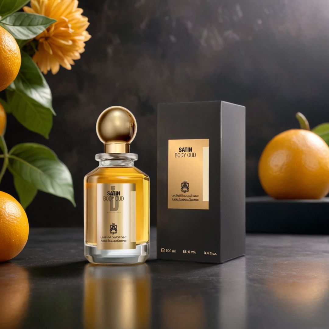The Satin Body Oud 100ml EDP by Abdul Samad Al Qurashi, with a gold cap, stands next to its elegant black and gold box. Fresh oranges and green leaves in the background highlight this long-lasting fragrance on a dark surface.