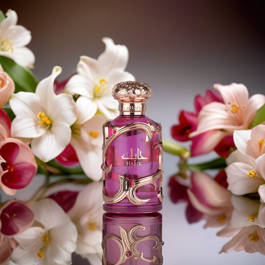 The Habik Women 100ml EDP by Lattafa features a decorative pink bottle with gold accents, set on a reflective surface amid blooming white and pink lilies, capturing the elegance of this Lattafa fragrance.