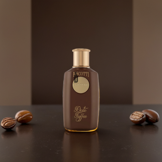 A bottle of Khadlaj Biscotti Date Toffee 100ml EDP with a gold cap rests on a dark surface amid coffee beans against a brown background—an inviting gourmand fragrance featuring caramel notes.