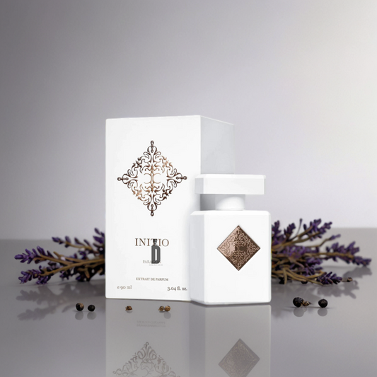 A white Paragon 90ml EDP bottle and box by Initio Parfums Prives are displayed on a reflective surface, accented by lavender and peppercorns, suggesting a spiritual, wisdom-inspired fragrance.