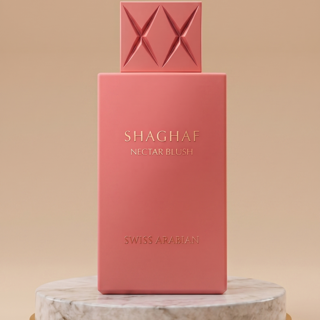 A pink rectangular 100ml bottle of Shaghaf Nectar Blush EDP by Swiss Arabian, with a diamond-like cap, stands upright on a round marble surface against a soft beige background.