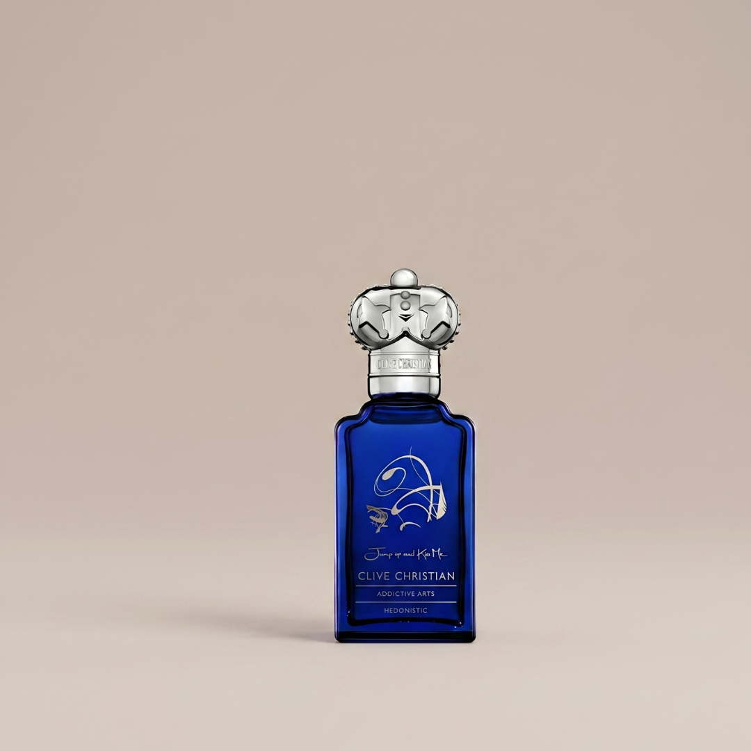 The Clive Christian Jump Up And Kiss Me Hedonistic 50ml EDP features a deep blue bottle with a silver crown-shaped cap, gold accents, and elegant script, set against a plain beige background.