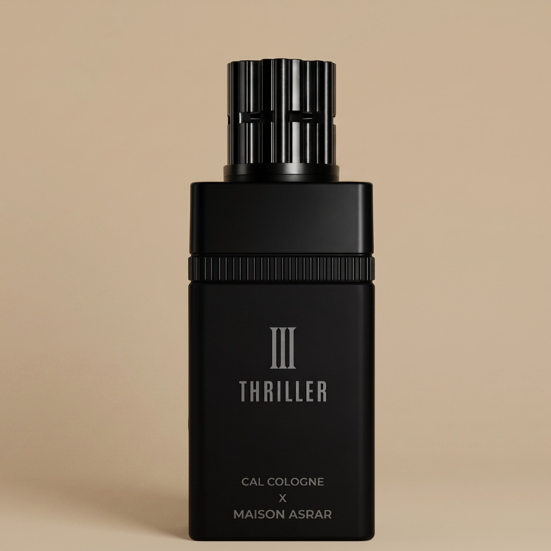 A black rectangular bottle of Thriller III 100ml EDP by Gulf Orchid stands upright against a beige background. With "III Thriller" on the label, its textured cylindrical cap adds elegance to this bold Maison Asrar x Cal Cologne fragrance for men.