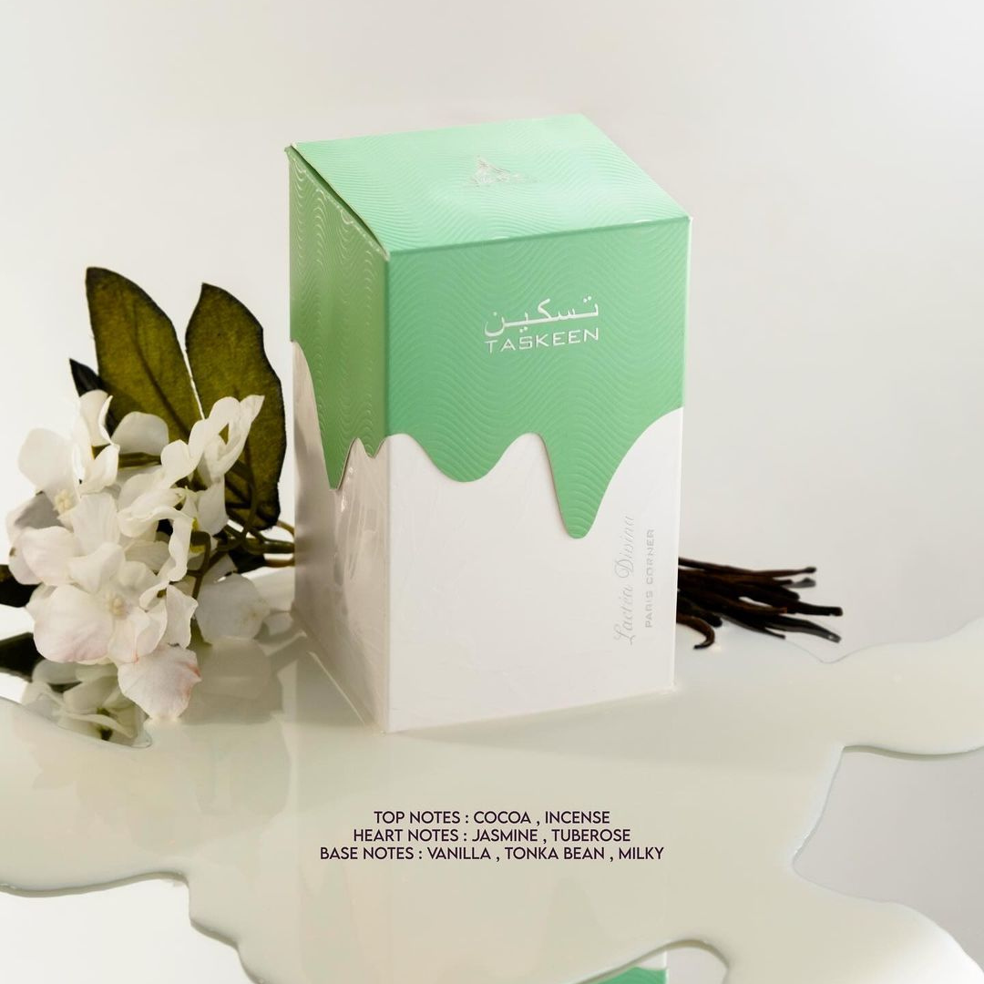 The perfume box for the "Taskeen Lactéa Divina 100ml EDP - Paris Corner" features a striking green and white design, beautifully presented with dark branches and white flowers to evoke a floral symphony. This luxurious fragrance by Paris Corner highlights top notes of cocoa and incense, heart notes of jasmine and tuberose, and base notes of vanilla, tonka bean, and creamy milk.