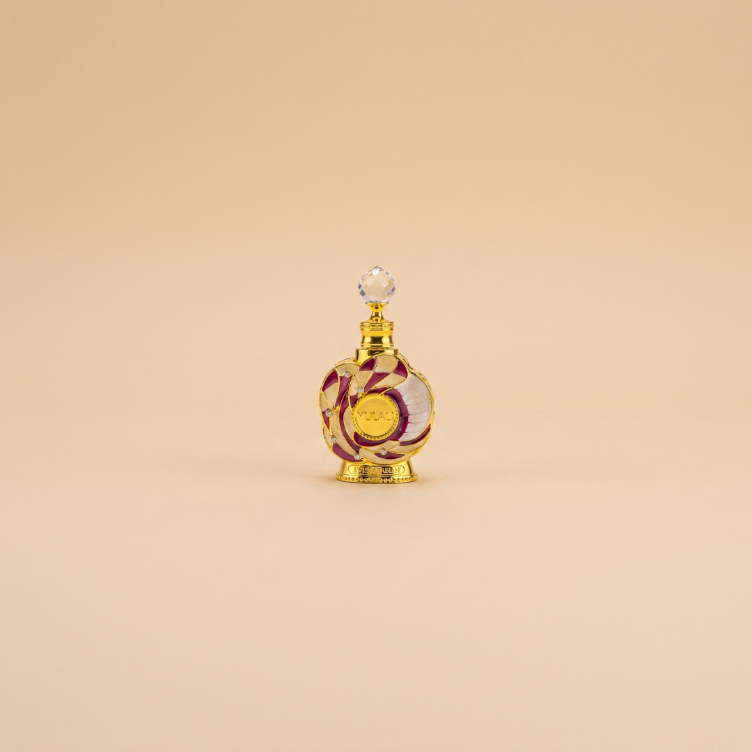 A 15ml bottle of Swiss Arabian Yulali Perfume Oil, featuring decorative gold and red detailing with a round crystal stopper, is displayed centered on a plain beige background.