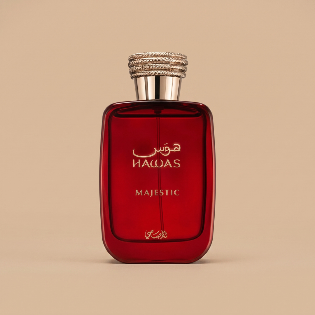 A bottle of “Hawas Majestic 100ml EDP” by Rasasi, featuring a striking red design with a metallic cap and gold Arabic script, is showcased against a plain beige background—conveying elegance and sophistication while suggesting the fresh scent inside.