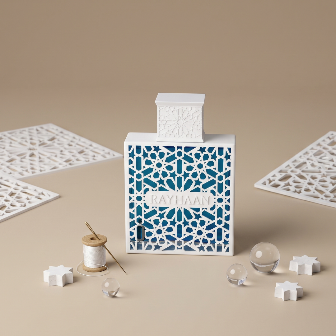 A decorative "Azul 100ml EDP - Rayhaan" perfume bottle featuring white geometric patterns, displayed with glass spheres, stars, thread, and patterned cards on beige—ideal for those who love fresh scents from Rayhaan.
