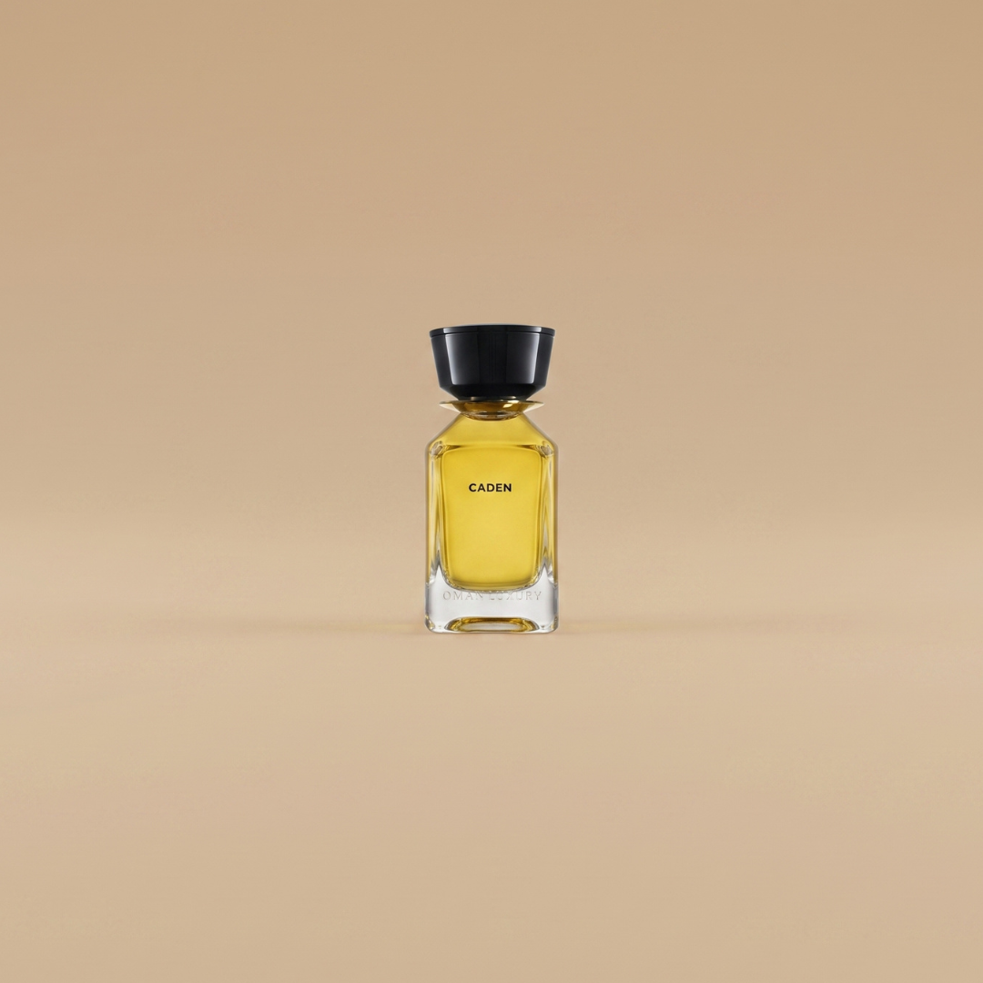 A transparent glass bottle labeled “Caden” with yellow liquid and a black cap, photographed against a solid beige background, displays the OmanLuxury Caden 100ml EDP—a sophisticated fragrance by OmanLuxury.