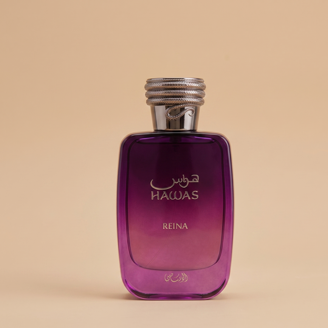 A purple glass perfume bottle labeled "Hawas Reina 100ml EDP - Rasasi" with silver accents and Arabic script stands against a beige background, reflecting its long-lasting gourmand floral fragrance from Rasasi.