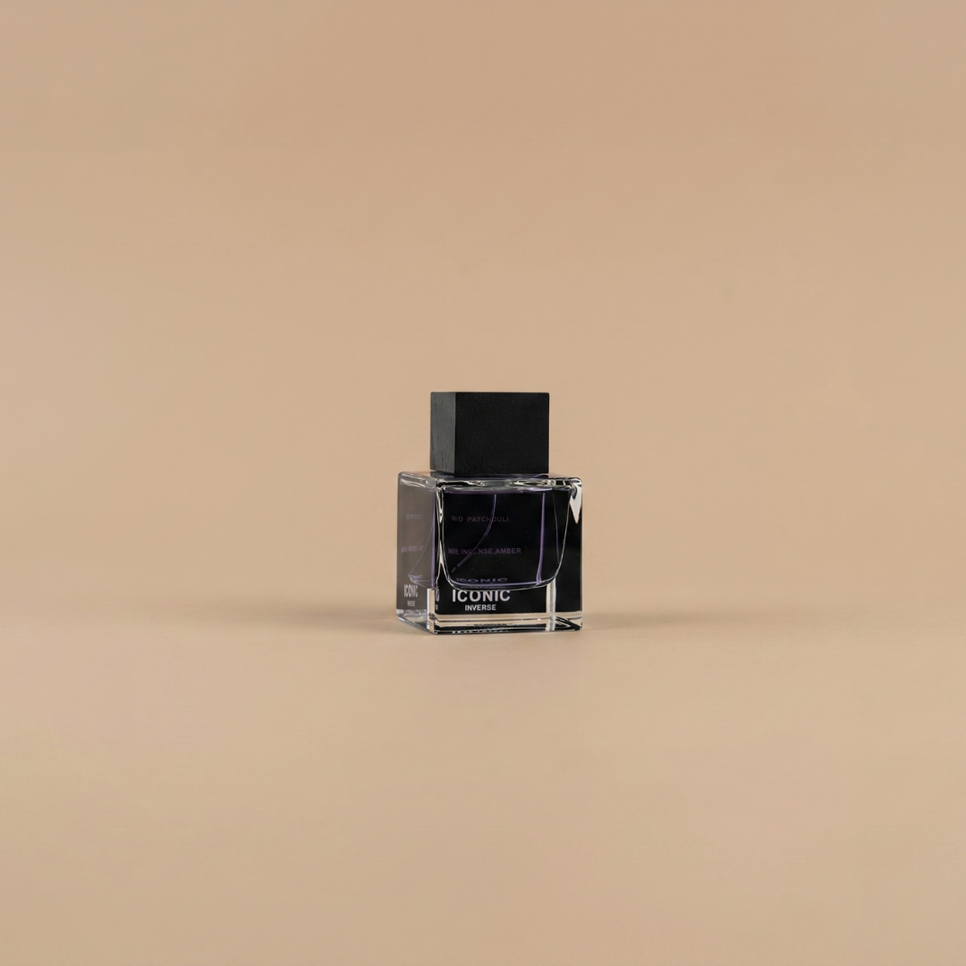 A transparent glass bottle of “Iconic Inverse 100ml EDP” by Aurora Scents, featuring a black cap and label reading “ICONIC,” is displayed on a light brown surface. This fresh marine fragrance from Aurora Scents is an ideal men’s scent for those who value timeless sophistication.