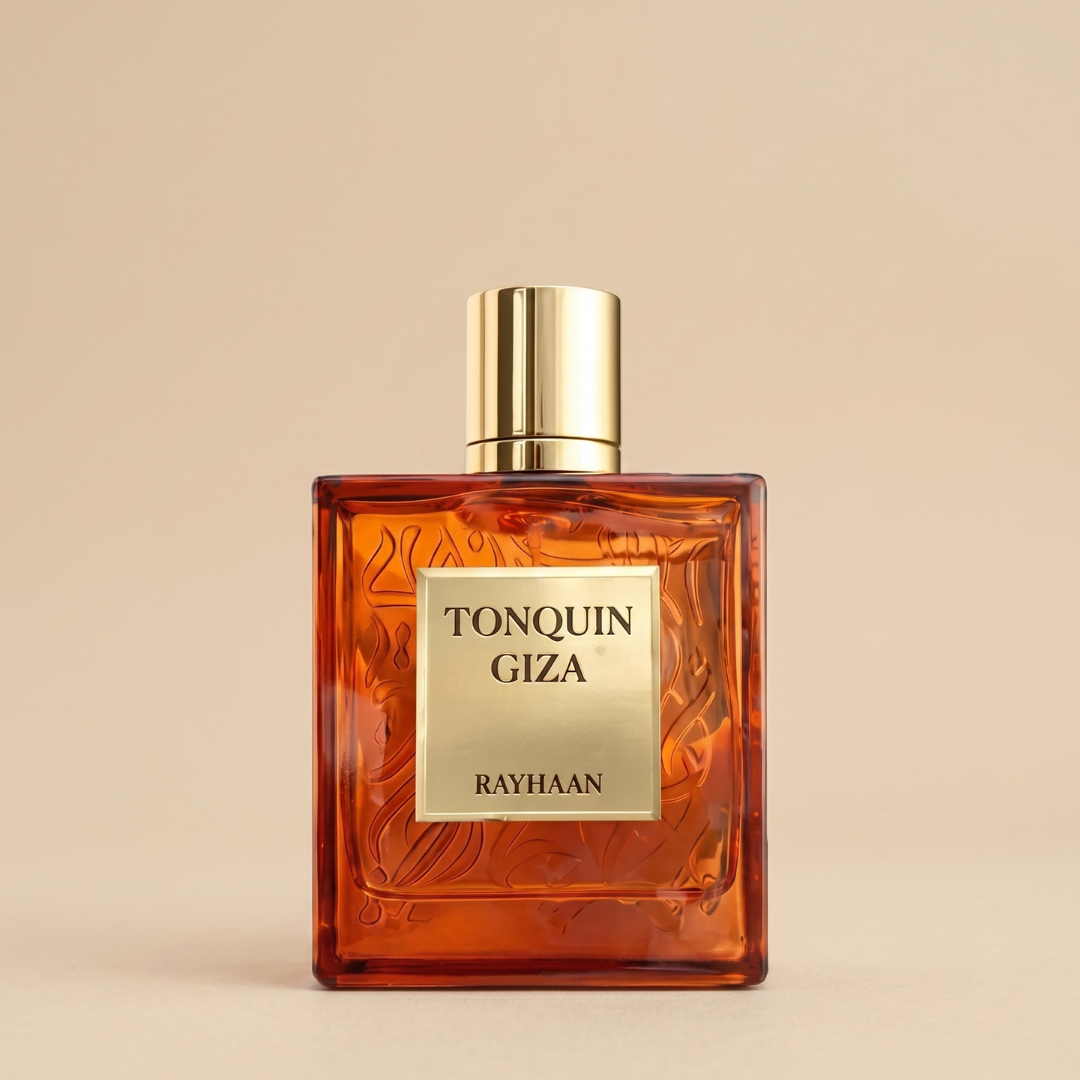 A square amber glass bottle of Tonquin Giza 100ml EDP by Rayhaan, with a gold cap and label, is set against a beige background and evokes a gourmand scent of tonka bean blended with creamy vanilla notes.
