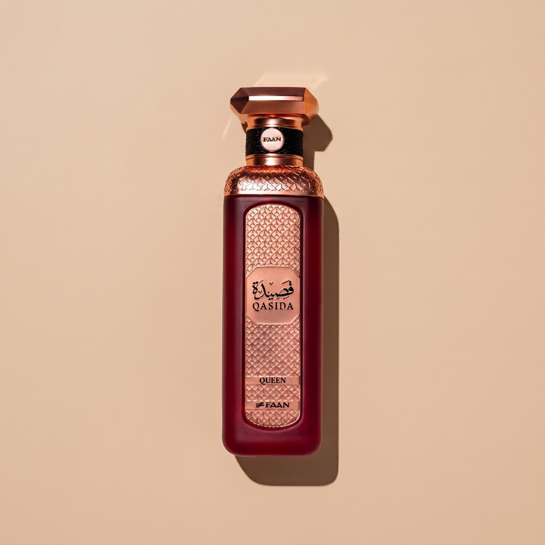 A luxurious 200ml perfume bottle labeled “Qasida Queen 200ml EDP - Faan Perfumes,” adorned with intricate gold detailing and Arabic script, is set against a plain beige background. This elegant creation from Faan Perfumes features an ornate design that hints at the captivating cherry fragrance within.