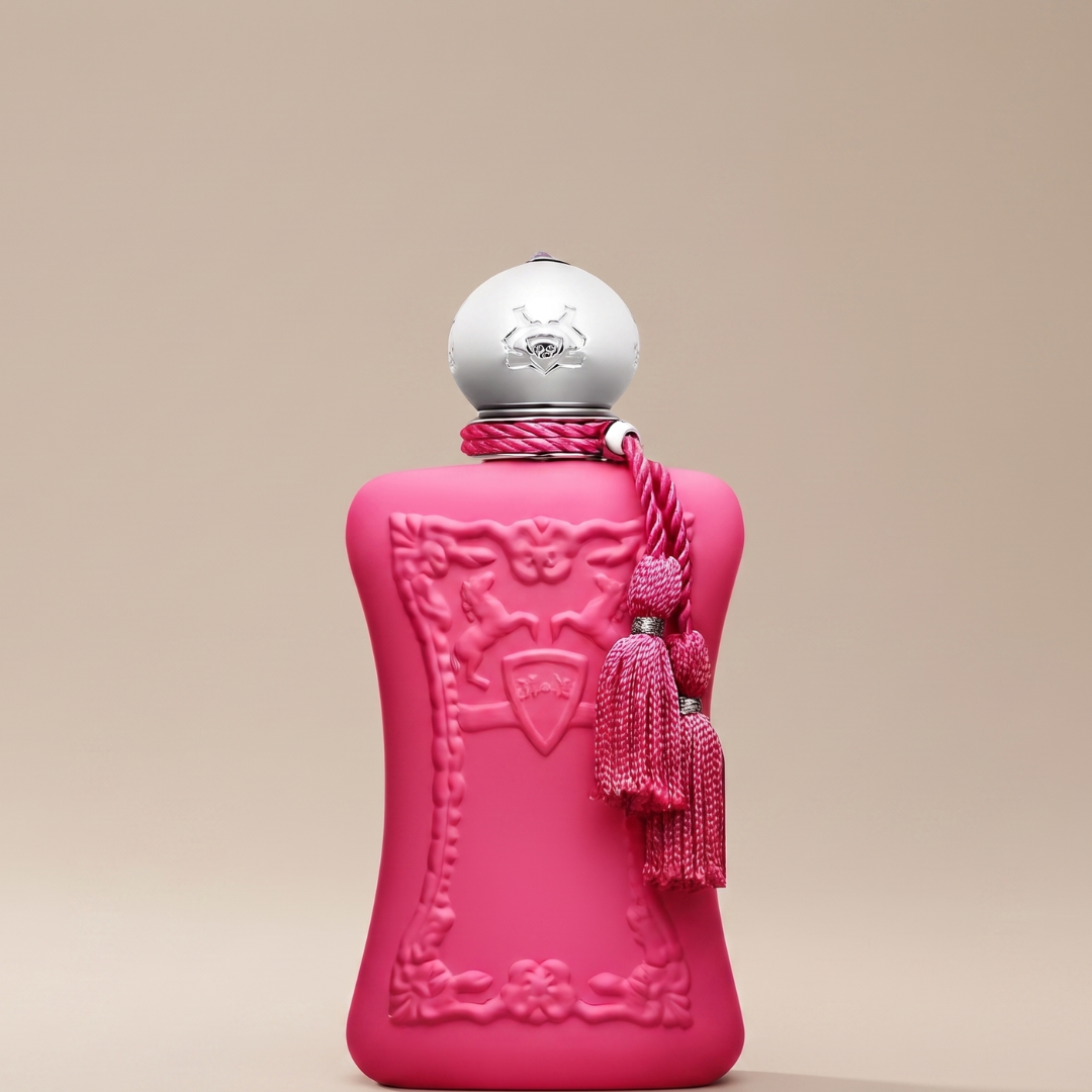 A pink perfume bottle with ornate detailing, a silver cap, and pink tassels stands upright against a neutral beige background, capturing the refined elegance of Oriana 75ml EDP by Parfums De Marly. This luxurious fragrance radiates sophistication and charm, making it an exquisite addition to any dressing table.