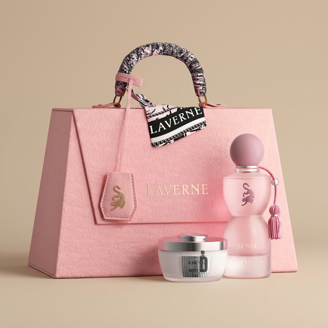 A pink Laverne gift bag with a patterned handle is shown next to the Sense Collection 75ml EDP - Laverne, a delicate and feminine fragrance by Laverne, and a silver-lidded cream jar, all set against a beige background.