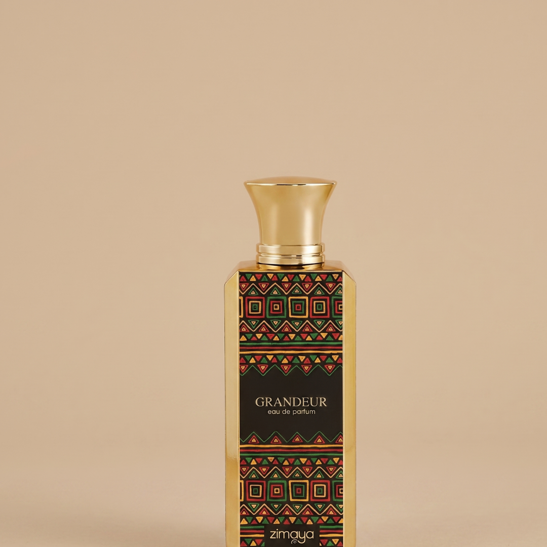 A gold perfume bottle adorned with a geometric, colorful pattern and the label "GRANDEUR eau de parfum" stands upright against a beige background. This exquisite floral gourmand fragrance, Grandeur 100ml EDP by Afnan, features "zimaya" at the bottom of the bottle and captivates with its elegant presence.