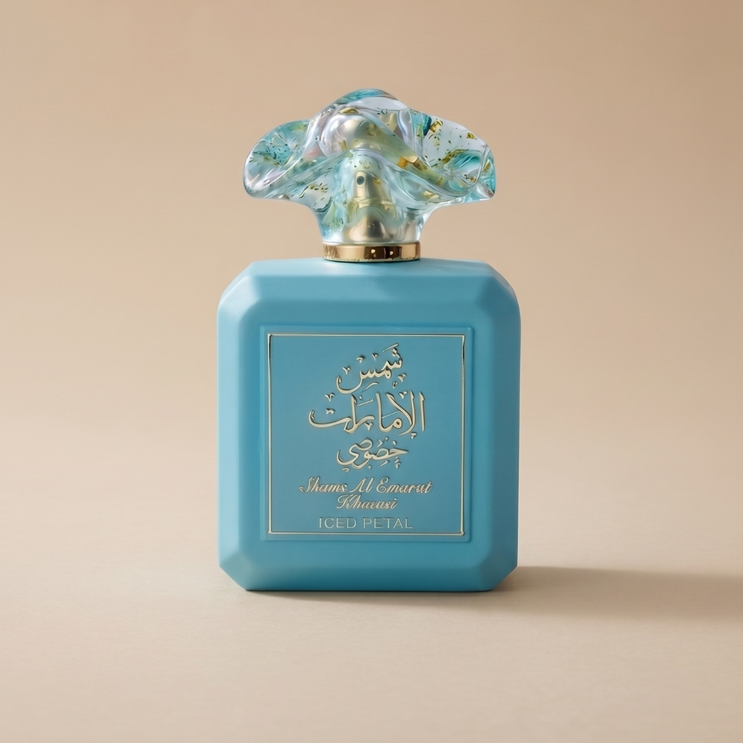 A blue 100ml Eau De Parfum bottle of Shams Al Emarat Khususi Iced Petal by Ard Al Zaafaran, featuring a decorative floral-patterned cap and gold Arabic and English text, is set against a beige background.